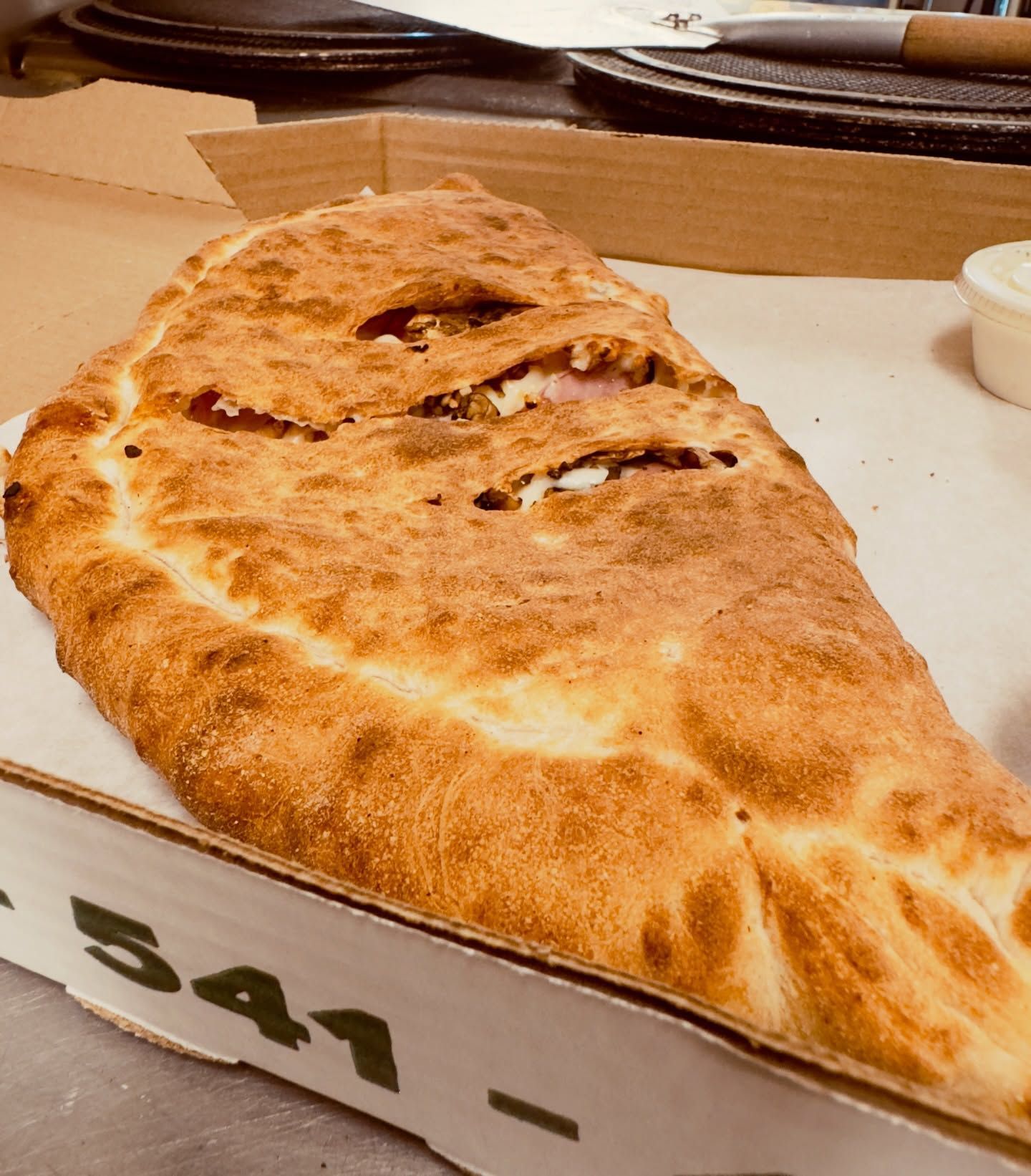 Golden-brown calzone on a takeout box with a white dipping cup on a table