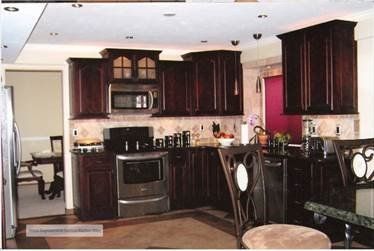 A kitchen featuring dark wood cabinets, stainless steel appliances, and a tiled backsplash, with a dining area nearby.