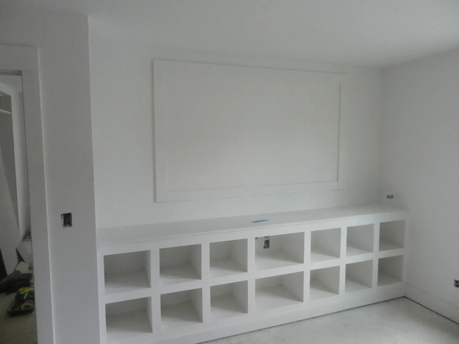White wall with a rectangular recessed panel and a white built-in storage unit featuring sixteen square open compartments.