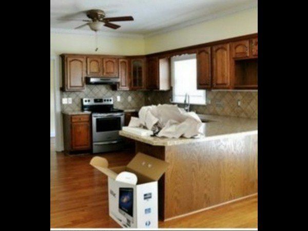 A kitchen with wooden cabinets, stainless steel appliances, a light-colored countertop, and a large box on the floor.