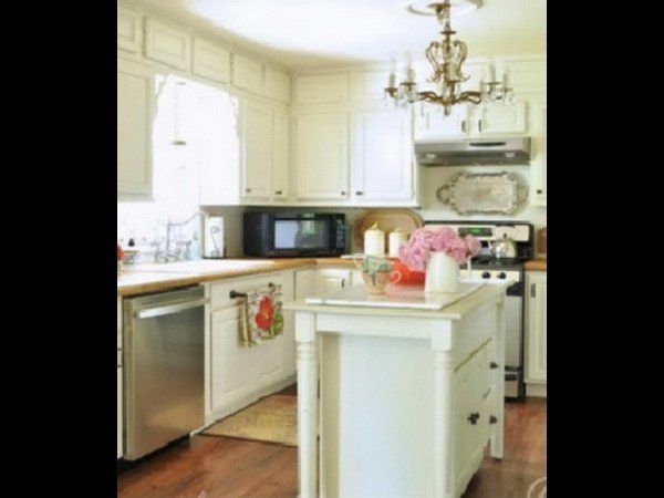 A kitchen with white cabinets, wood floors, a stainless steel dishwasher, a microwave, and a small center island.