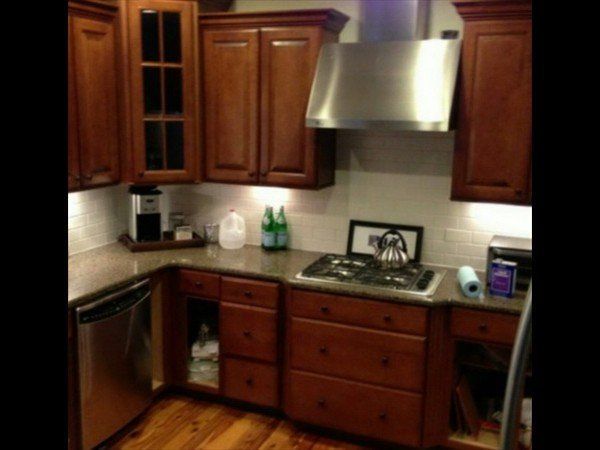 A kitchen featuring wood cabinets, stainless steel appliances, a stovetop, and a vent hood over a countertop.