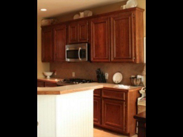 A kitchen with warm-toned wood cabinets, a stainless steel microwave, and a white beadboard kitchen island.