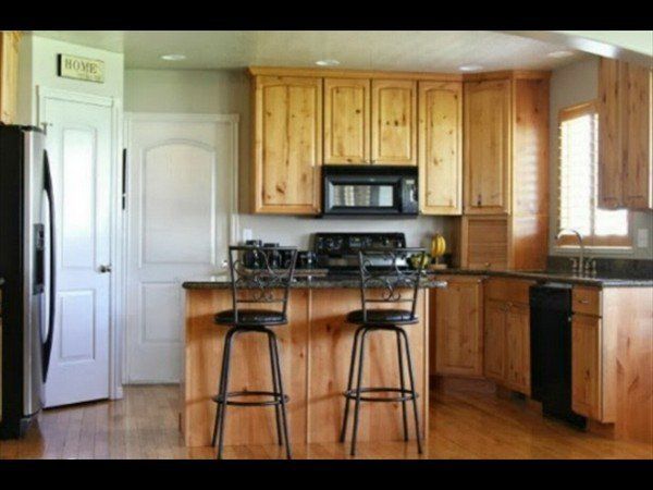 A kitchen with light wood cabinets, black appliances, a central island with two bar stools, and a window with shutters.