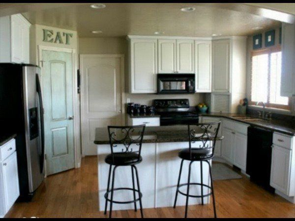 A bright, modern kitchen featuring white cabinets, black appliances, a small island with two stools, and wood flooring.