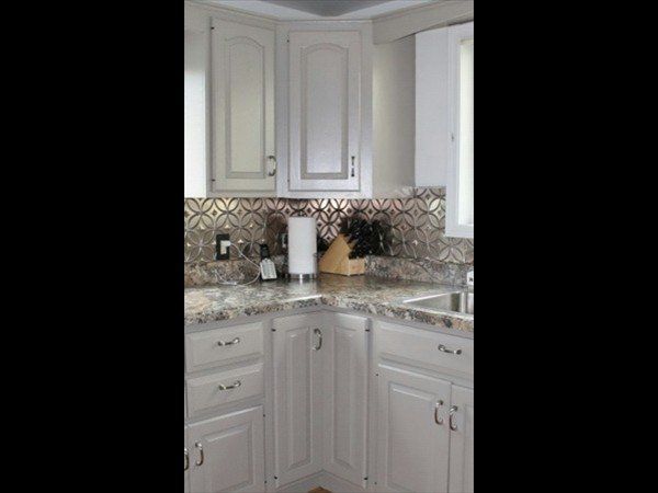 A corner kitchen view with light grey cabinets, a patterned tile backsplash, and light stone countertops.