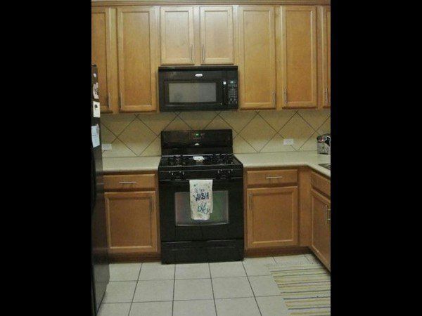Kitchen with light wood cabinets, black appliances, tan countertops, and a diagonal tile backsplash.