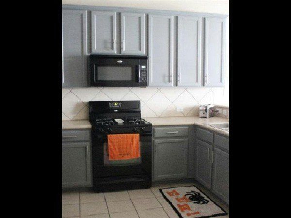 A kitchen with grey cabinets, a black microwave and stove, a light countertop, and a tiled floor with a small rug.