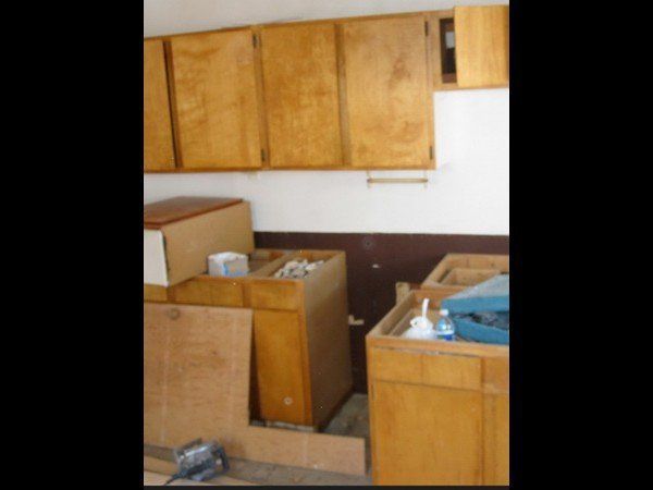 A kitchen undergoing renovation with unfinished wooden upper cabinets, base cabinets, and a partial brown-painted wall.