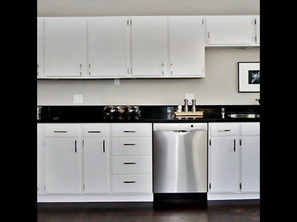 A kitchen featuring white cabinets, black countertops, and a stainless steel dishwasher.