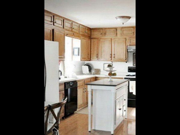A kitchen with light wood cabinets, white countertops, a central white island, and black appliances.