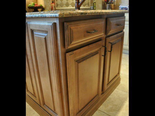 A kitchen island featuring medium-toned wood cabinetry with paneled doors, drawers, and a granite countertop.