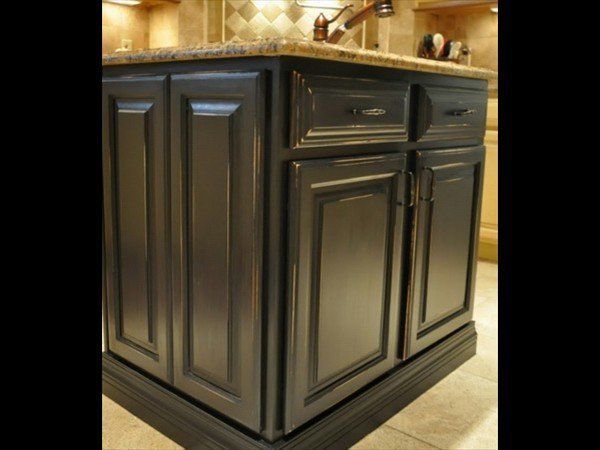 A dark gray kitchen island with a granite countertop, featuring cabinet doors and drawers in a classic raised-panel style.