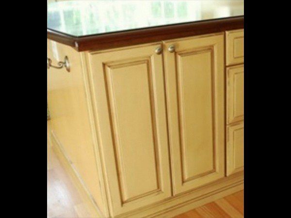 Cream-colored kitchen cabinets with dark wood-toned glazing and a dark countertop edge, shown at an angle.