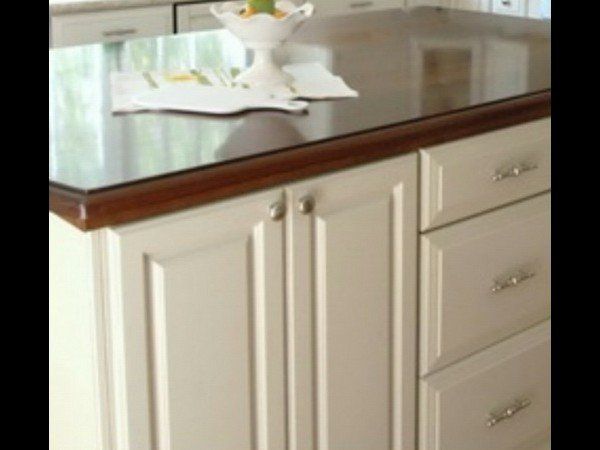 A white kitchen island with a dark wood edge, granite countertop, two cabinet doors, and three stacked drawers.