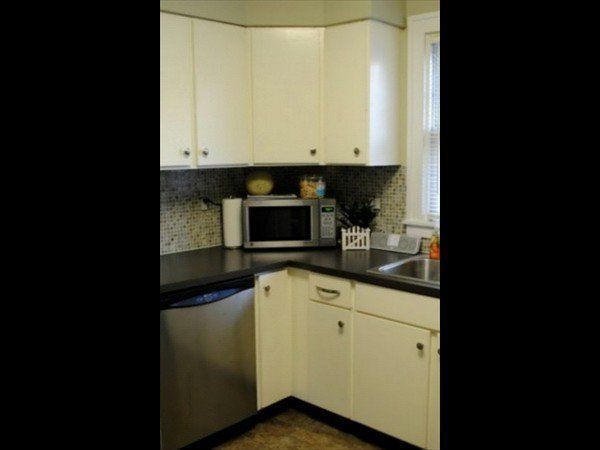 A kitchen corner with white cabinets, a black countertop, a stainless steel dishwasher, and a microwave on the counter.