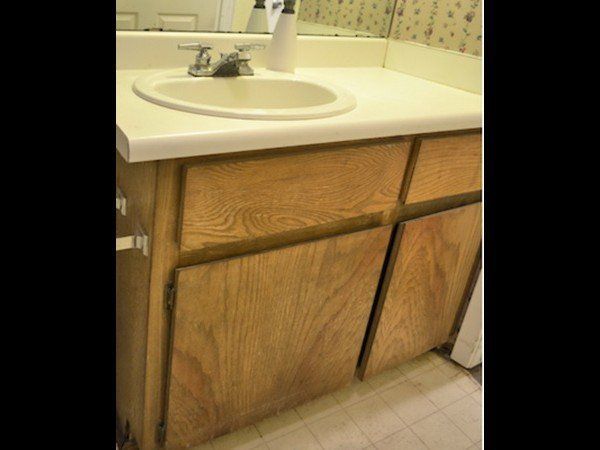 A bathroom vanity with a white countertop and sink, featuring light-colored wood cabinets and drawers.