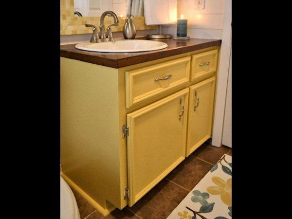 A yellow bathroom vanity with a dark brown countertop, a white oval sink, and metal hardware.
