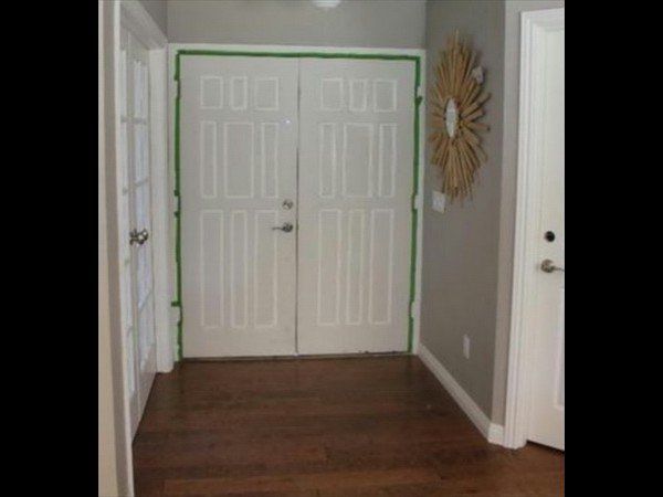 A set of double doors with green painter's tape on the frame, positioned in a hallway with dark wood floors and gray walls.