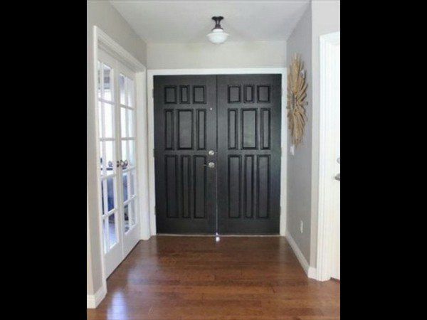 An interior entryway with hardwood floors, a central black double door, a glass-paned side door, and a modern light fixture.