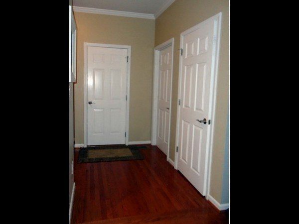 An interior hallway featuring dark wood floors, beige walls, and three white six-panel doors.
