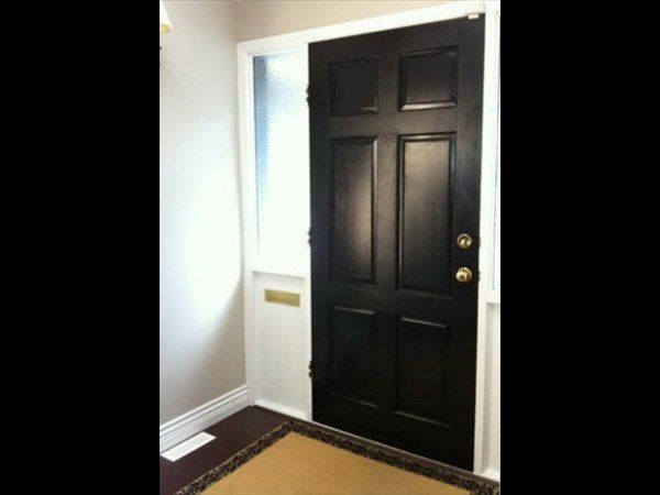 A black six-panel front door with brass hardware, set within a white frame next to a glass sidelight in an entryway.
