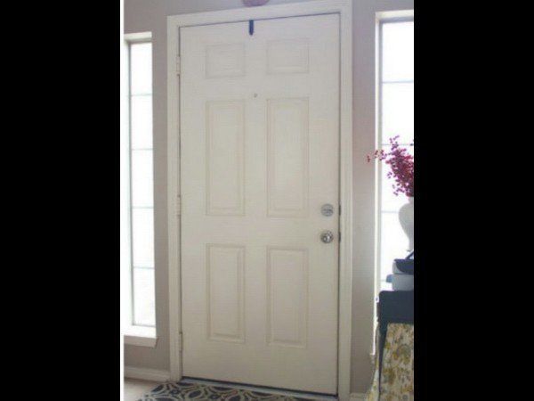 A white, four-panel front door with a peephole and silver hardware, flanked by vertical windows in a neutral-toned room.