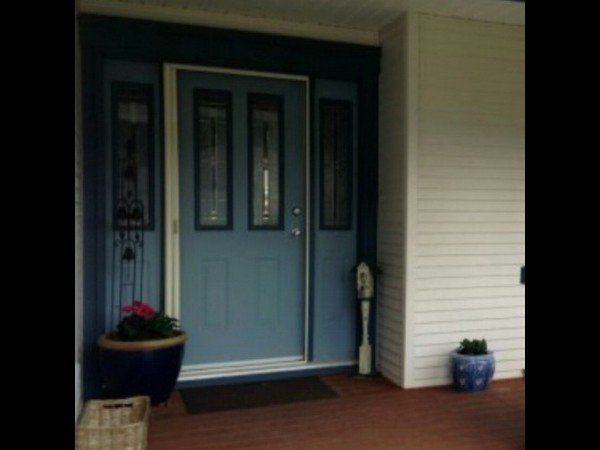 A front entrance with a blue door, sidelight windows, a blue potted plant on the left, and a small blue pot on the right.