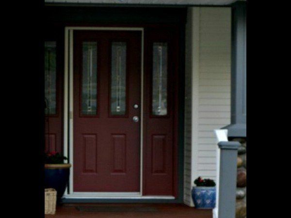 A dark red front door with two vertical glass panels, set in a light-colored home exterior with a nearby blue planter.