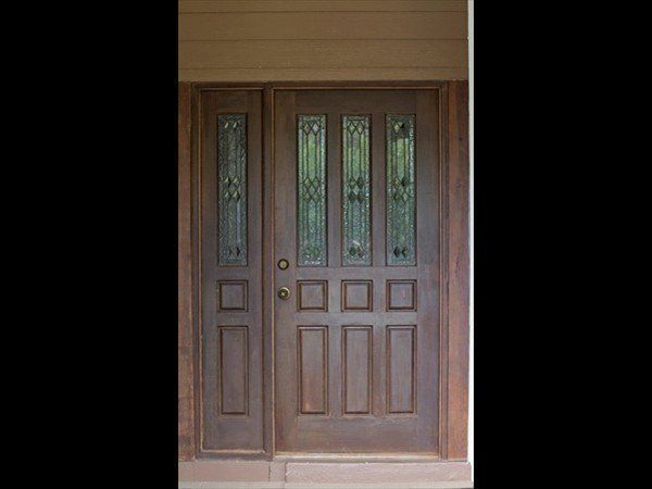 A brown wooden front door with four glass window panes and a matching side light panel.