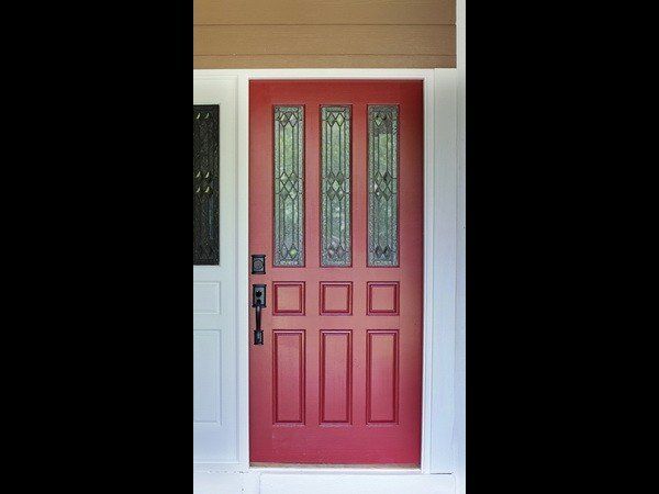 A red front door with three vertical glass panels and a black handle set, framed by white trim and a brown header.