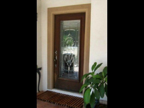 A dark wooden front door with a decorative glass panel, framed by stone molding, next to a potted green plant.