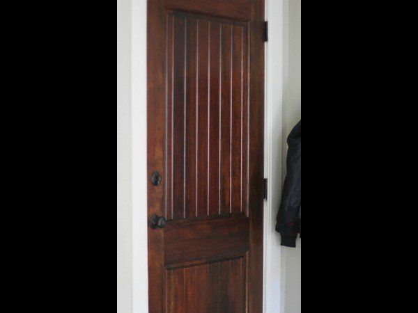 A dark wood door with vertical panels and a recessed bottom section, set in a white wall with a jacket hanging nearby.