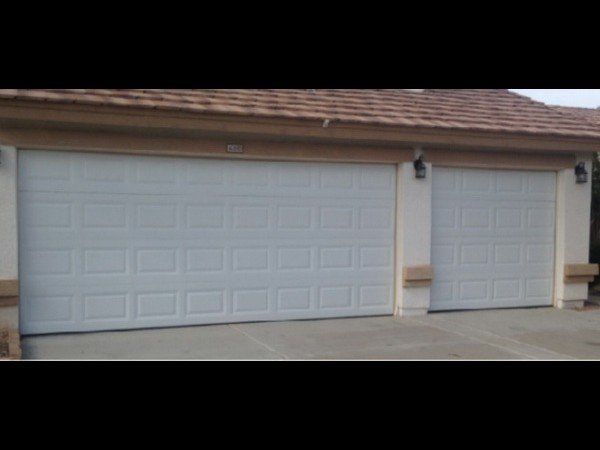 A tan exterior wall with a white double-car garage door and a smaller single-car garage door under a brown shingled roof.