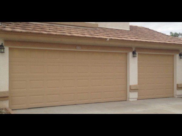 A beige two-car garage with horizontal paneling and brown shingle roofing on a house exterior.