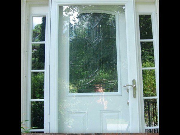 A white front door featuring a large glass pane with a decorative design, flanked by two narrow sidelight windows.