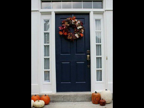 A navy blue front door with a fall wreath, flanked by white sidelights and decorated with pumpkins on the porch.
