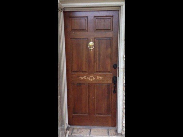 A brown wooden front door with six panels, a gold door knocker, and gold decorative trim in the center.