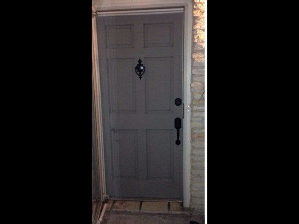 A grey six-panel front door with black hardware, including a door knocker, handle, and deadbolt, set in a stone wall.