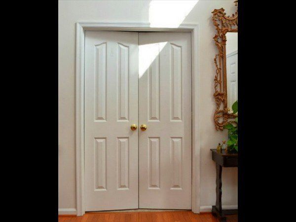 White double interior doors with gold knobs in a hall with a mirror and table to the right.