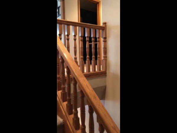 A wooden staircase with matching railings and balusters leads to an upper floor hallway with a dark, open doorway.