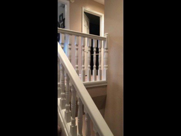 A white staircase railing leads upward toward a dimly lit hallway with open doorways in a residential home.