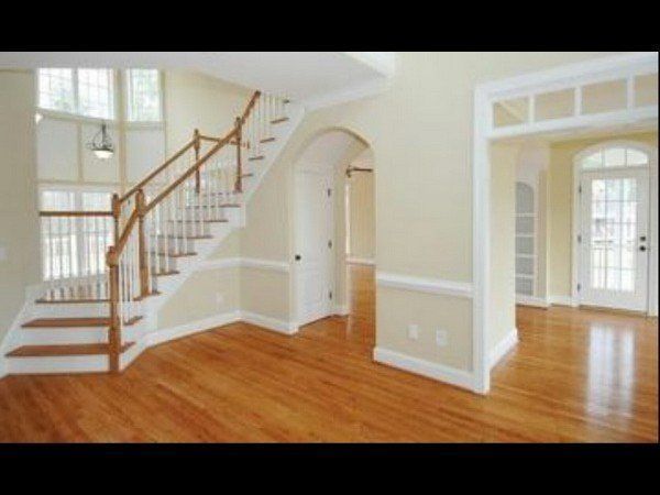 An empty foyer with light beige walls, a curved staircase with a wooden railing, hardwood floors, and a glass-paneled door.
