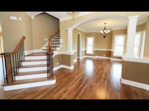 A bright foyer featuring a wooden staircase, hardwood floors, tan walls with white trim, and an arched entryway.