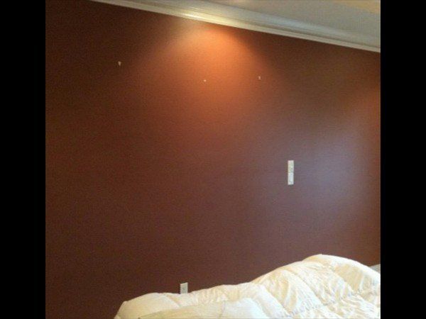 A solid brown bedroom wall with a light switch, crown molding, and a partial view of a white bedspread below.