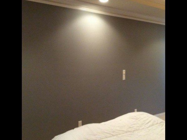 A dark gray bedroom wall with a light switch, crown molding, and part of a white bedspread in the foreground.