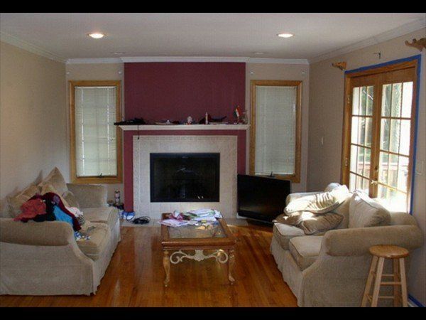 A living room featuring two beige sofas, a glass coffee table, and a fireplace with a maroon wall above it.