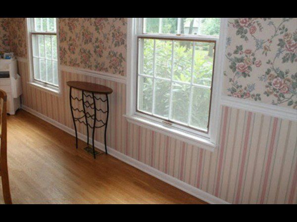 A room with hardwood floors, floral wallpaper above a chair rail, striped wallpaper below, and a metal wine rack.