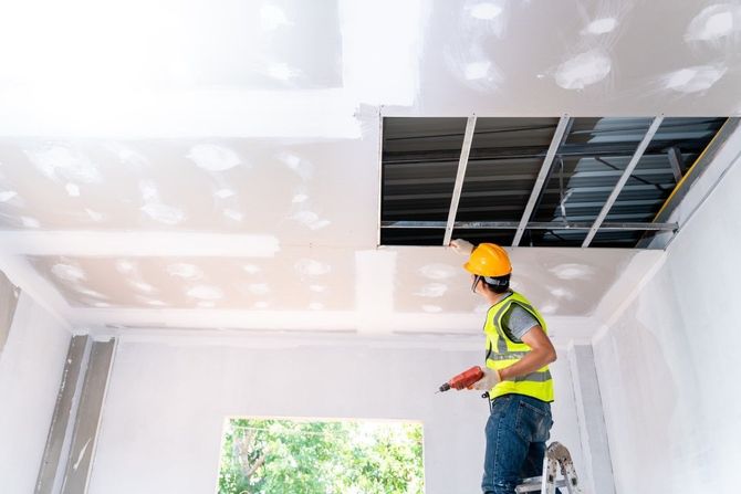 Professional worker installing drywall around a ceiling vent.