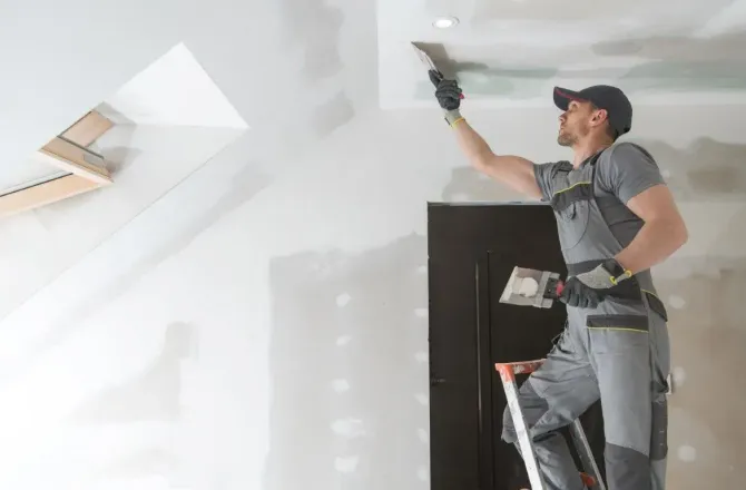 Drywall contractor finishing a door frame and ceiling edge.
